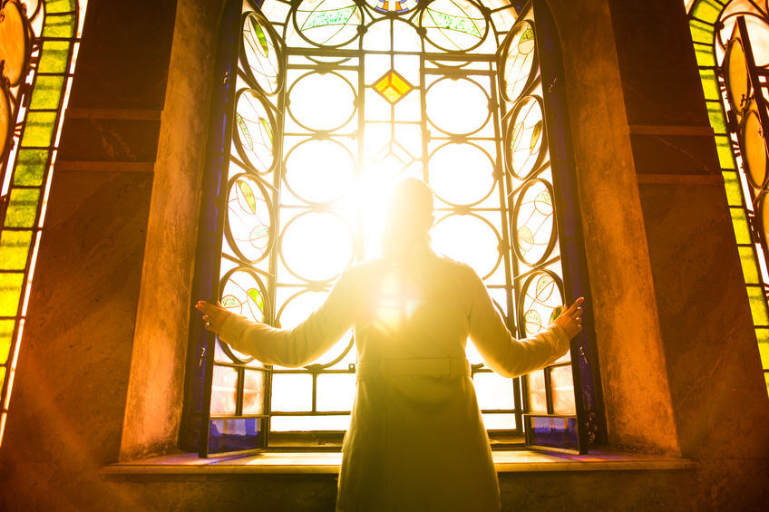 Religious woman in a church looking at the light shining through a stained glass window 