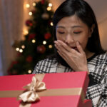 A woman opening a gif, covering her mouth in excitement